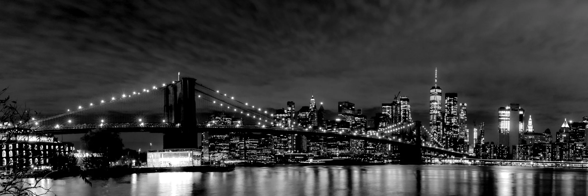 Black-and-white nighttime panorama of the Brooklyn Bridge and Manhattan skyline