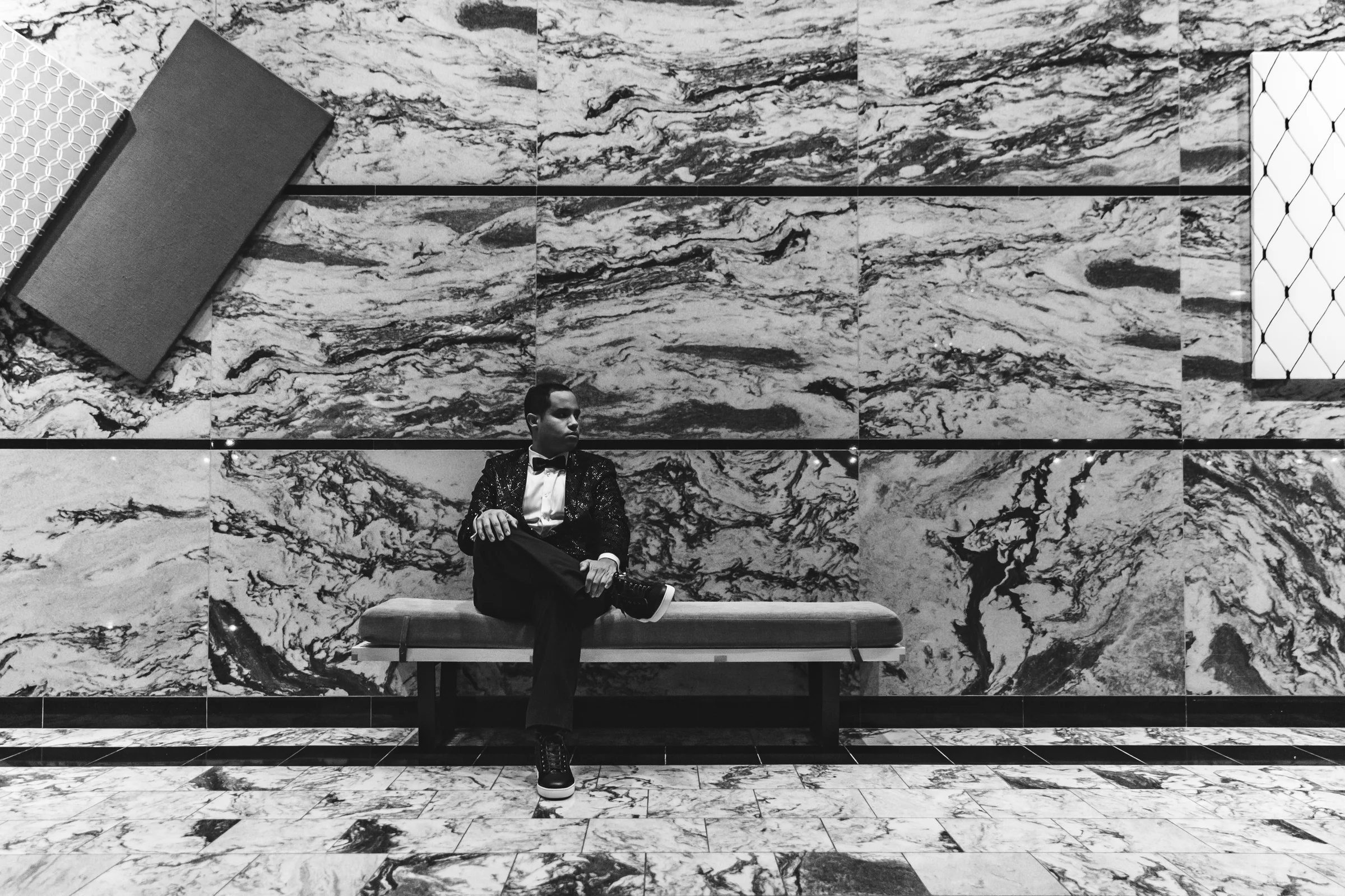 Black-and-white environmental portrait of a man seated against a marble wall