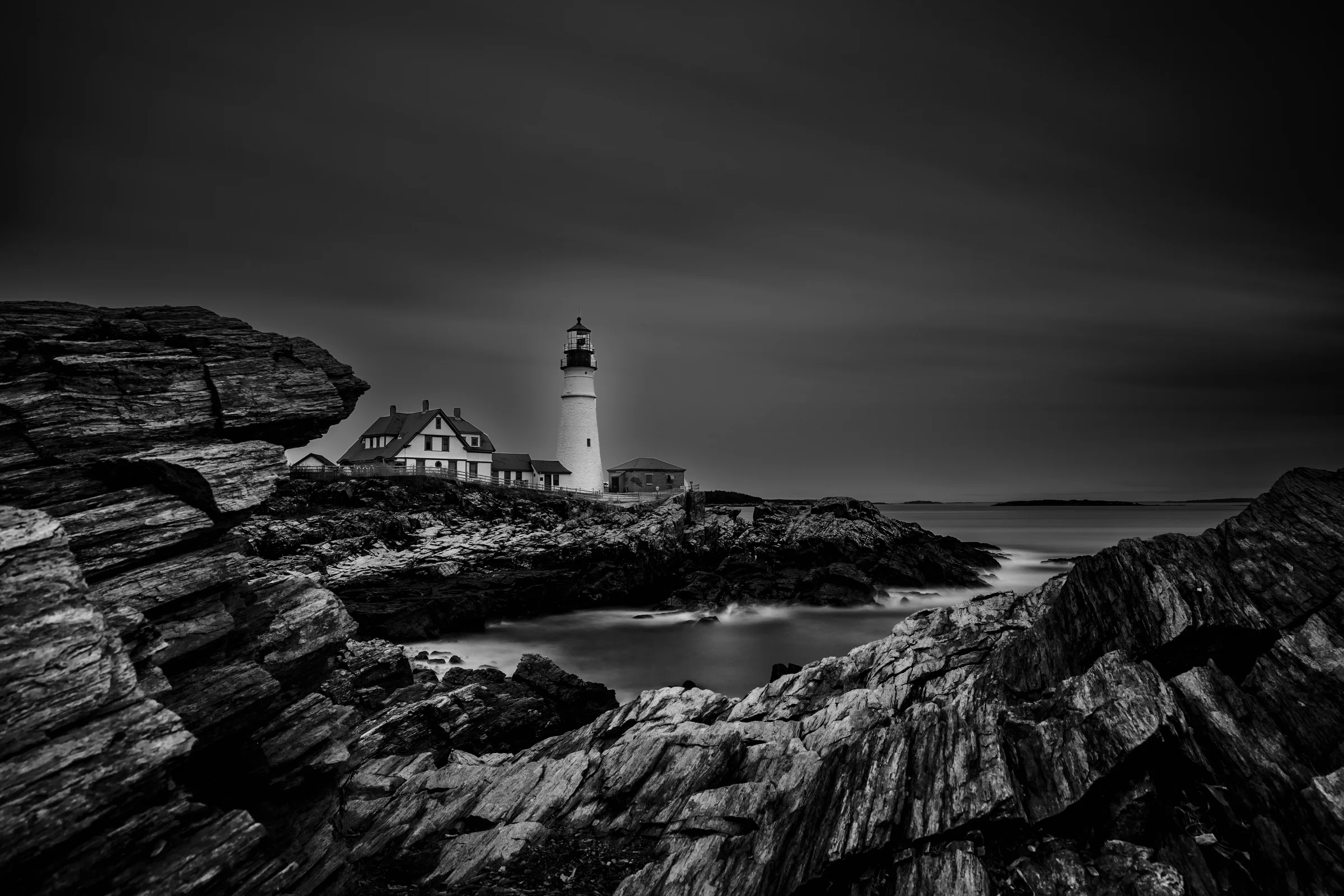 Long-exposure black-and-white photograph of a lighthouse on a rocky coast